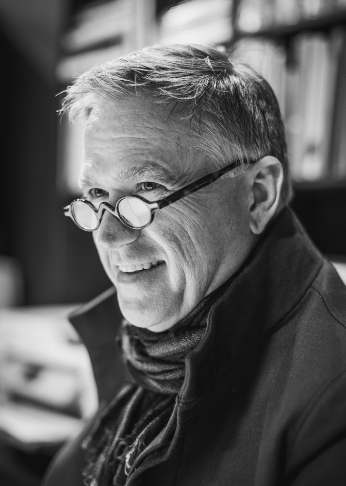Smiling elderly man with glasses in black and white portrait.