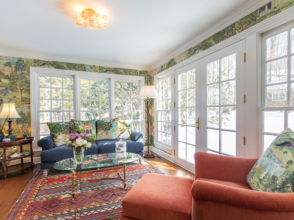Bright living room with large windows, blue sofa, and red armchair overlooking garden.