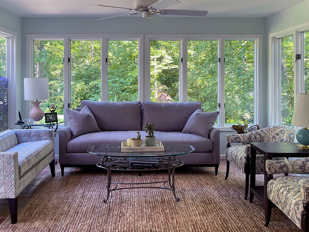 Cozy living room with a purple sofa and large windows overlooking greenery.