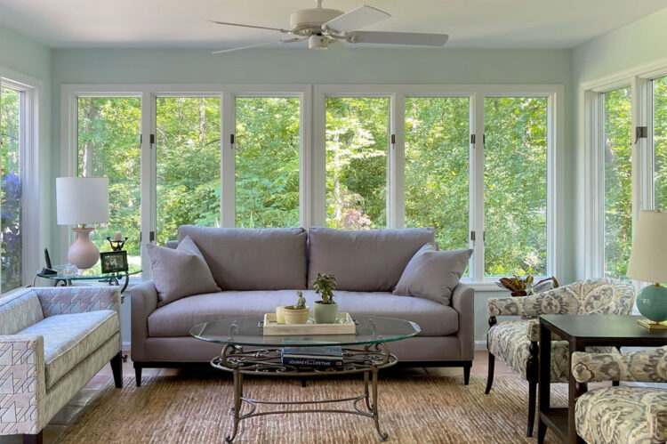 Elegant living room with a gray sofa and large windows showcasing lush greenery.