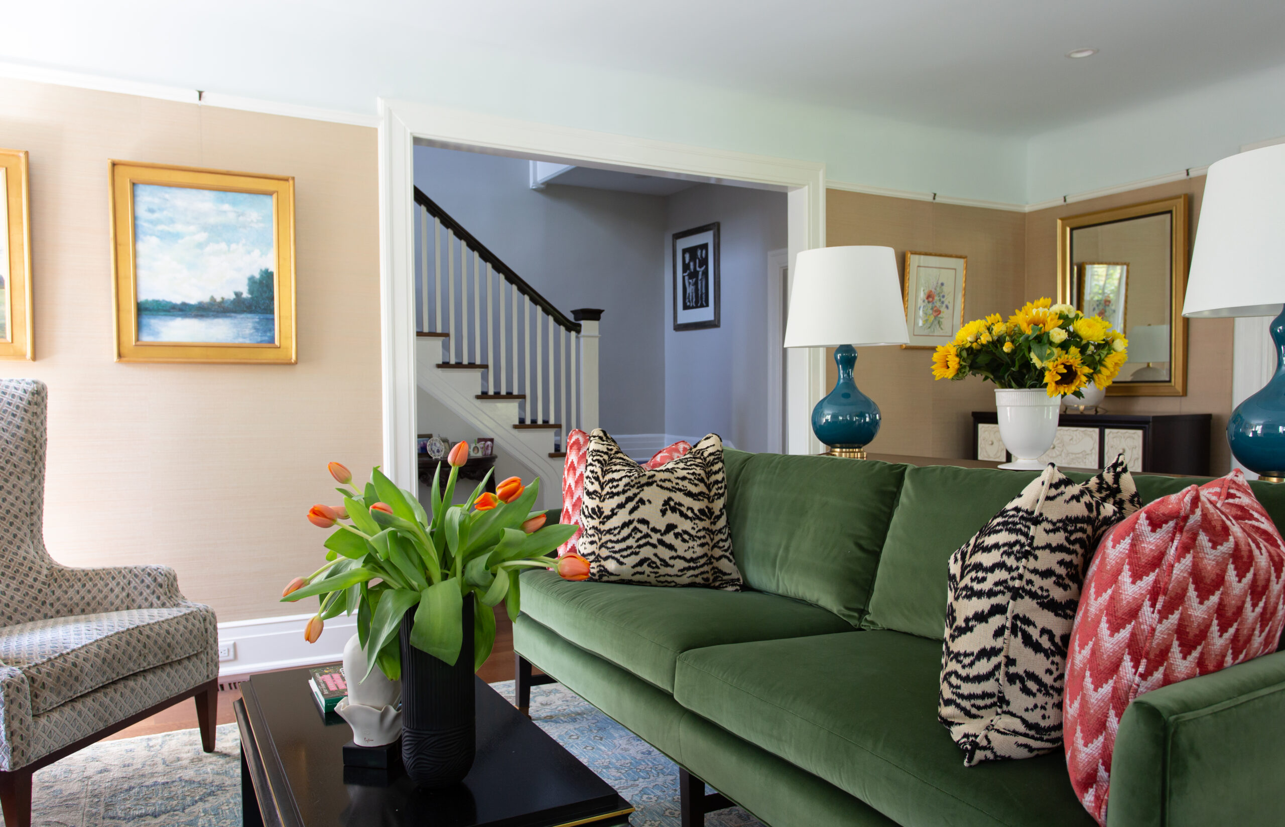 Cozy living room with green velvet sofa, patterned cushions, and fresh flowers.