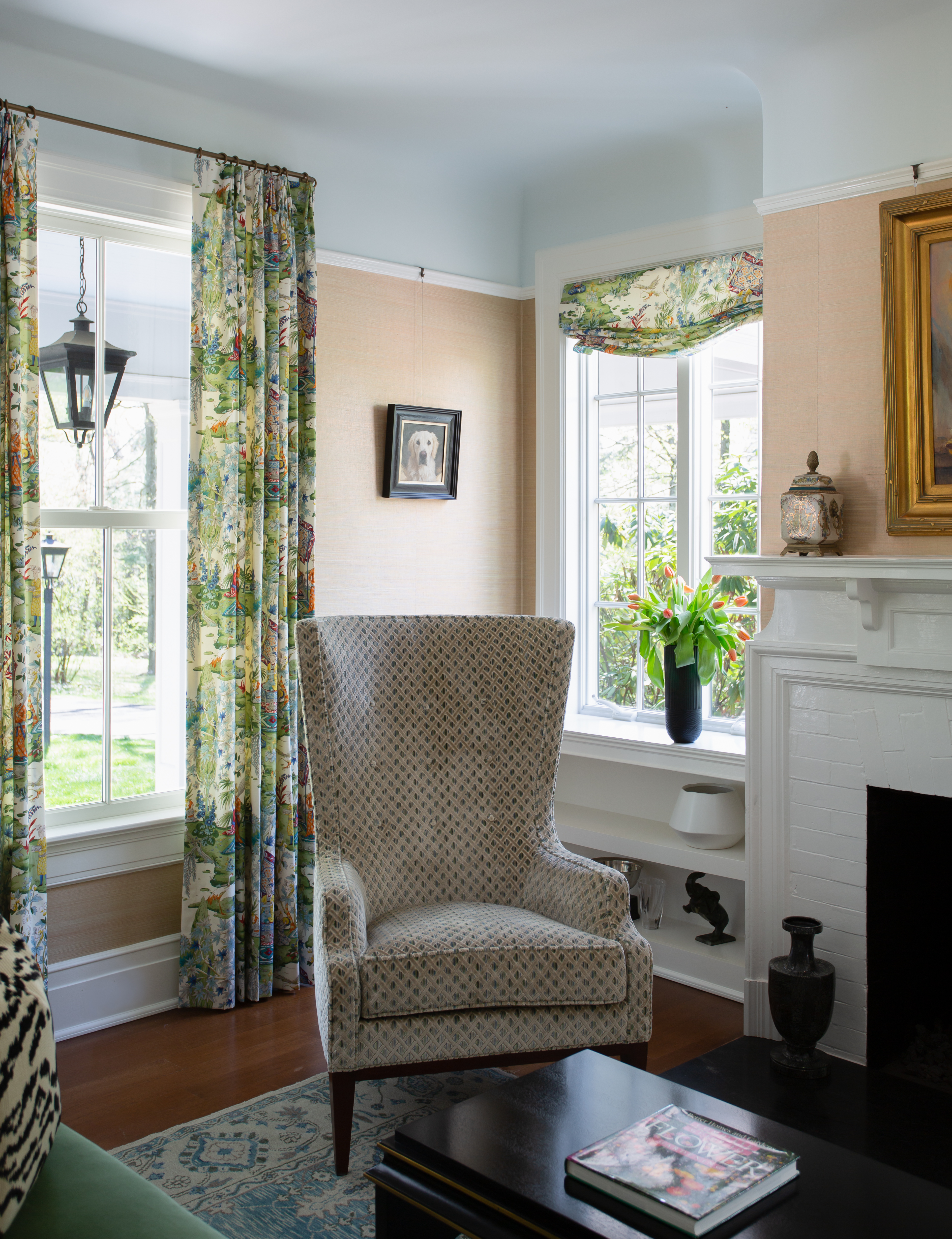 Cozy living room corner with patterned armchair, floral curtains, and a vase of tulips by the window.