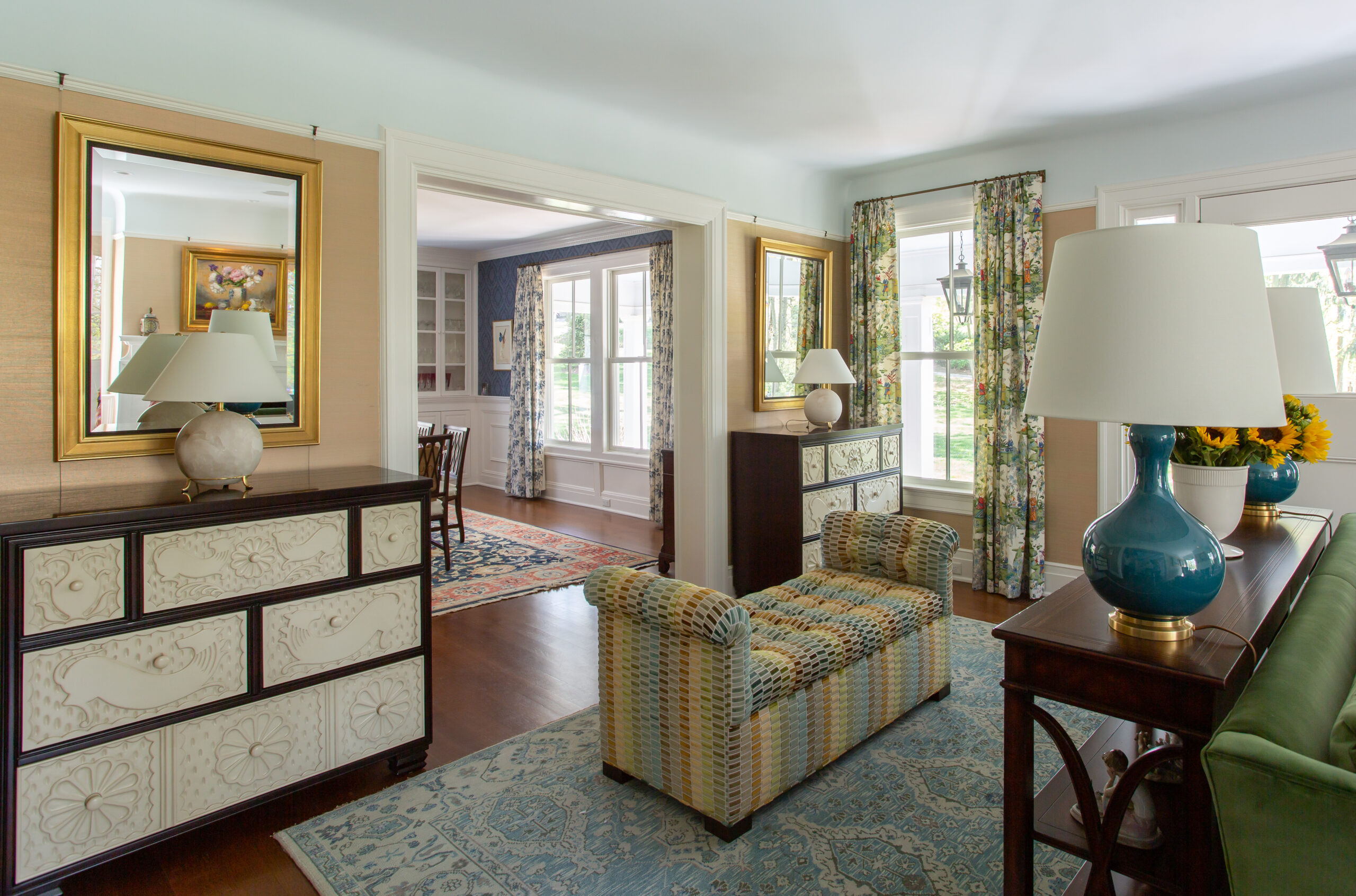 Elegant living room with patterned bench, floral curtains, and decorative lamps on wooden furniture.
