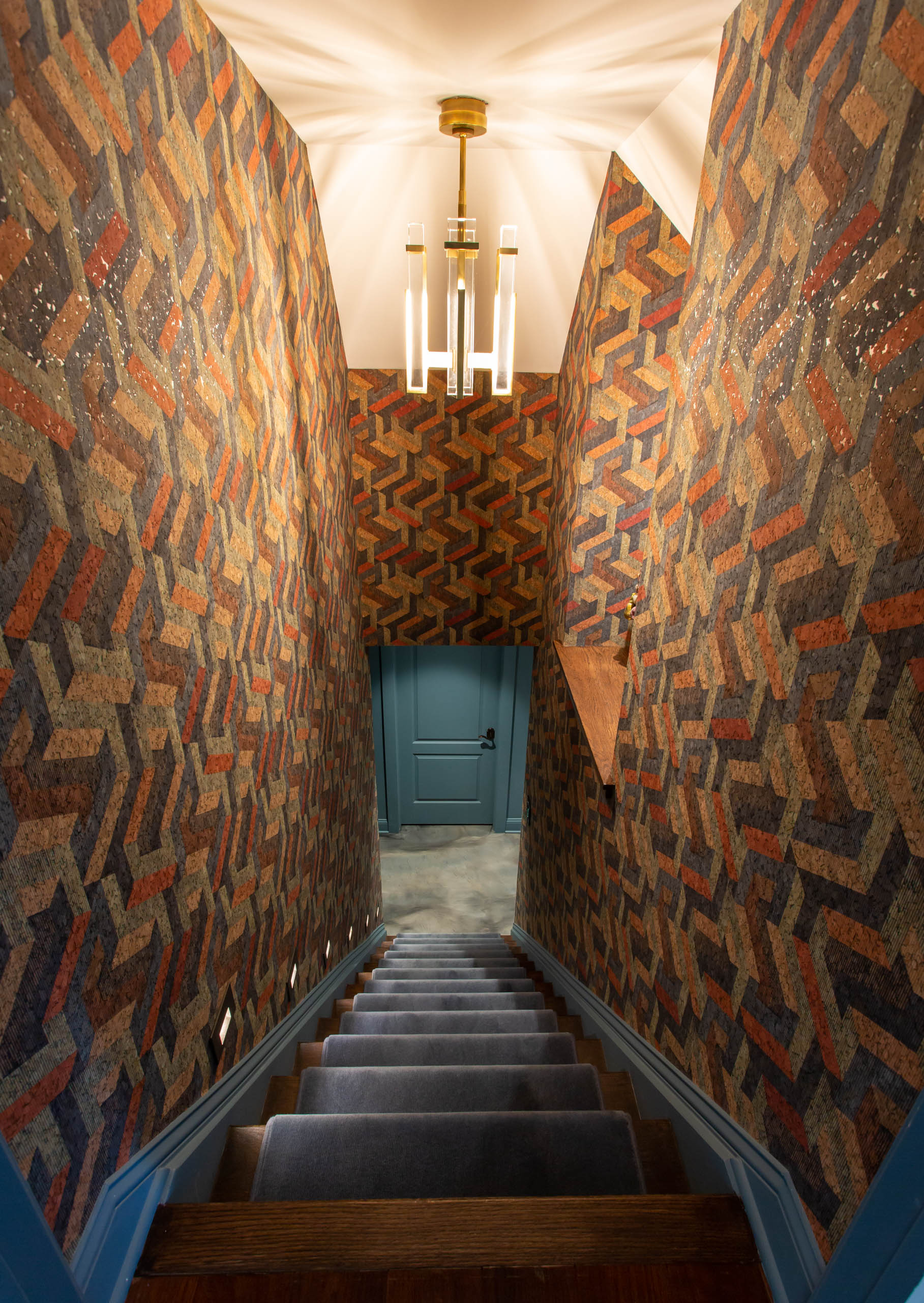 Narrow staircase with patterned walls and a blue door at the bottom.