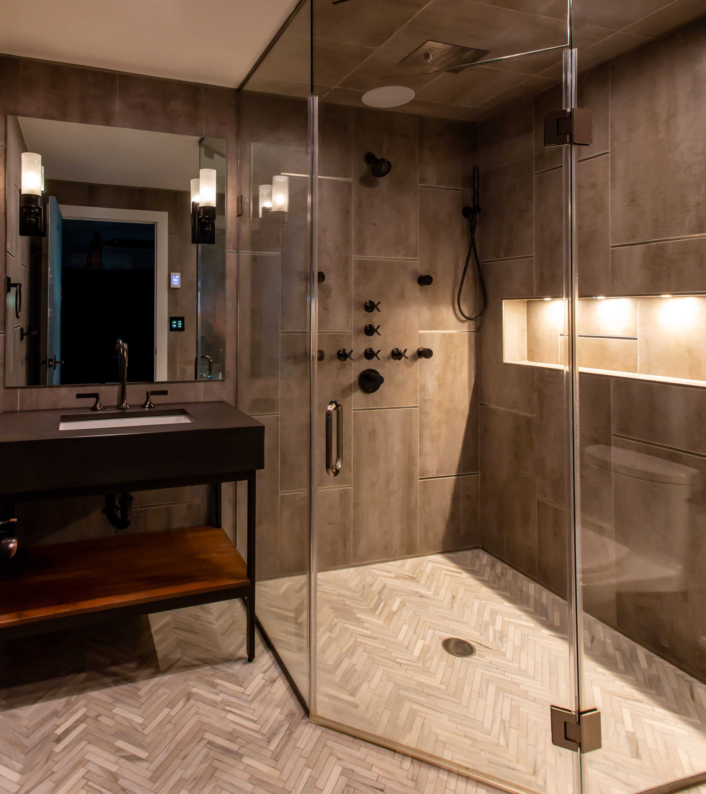 Modern bathroom with glass shower and herringbone tile floor.